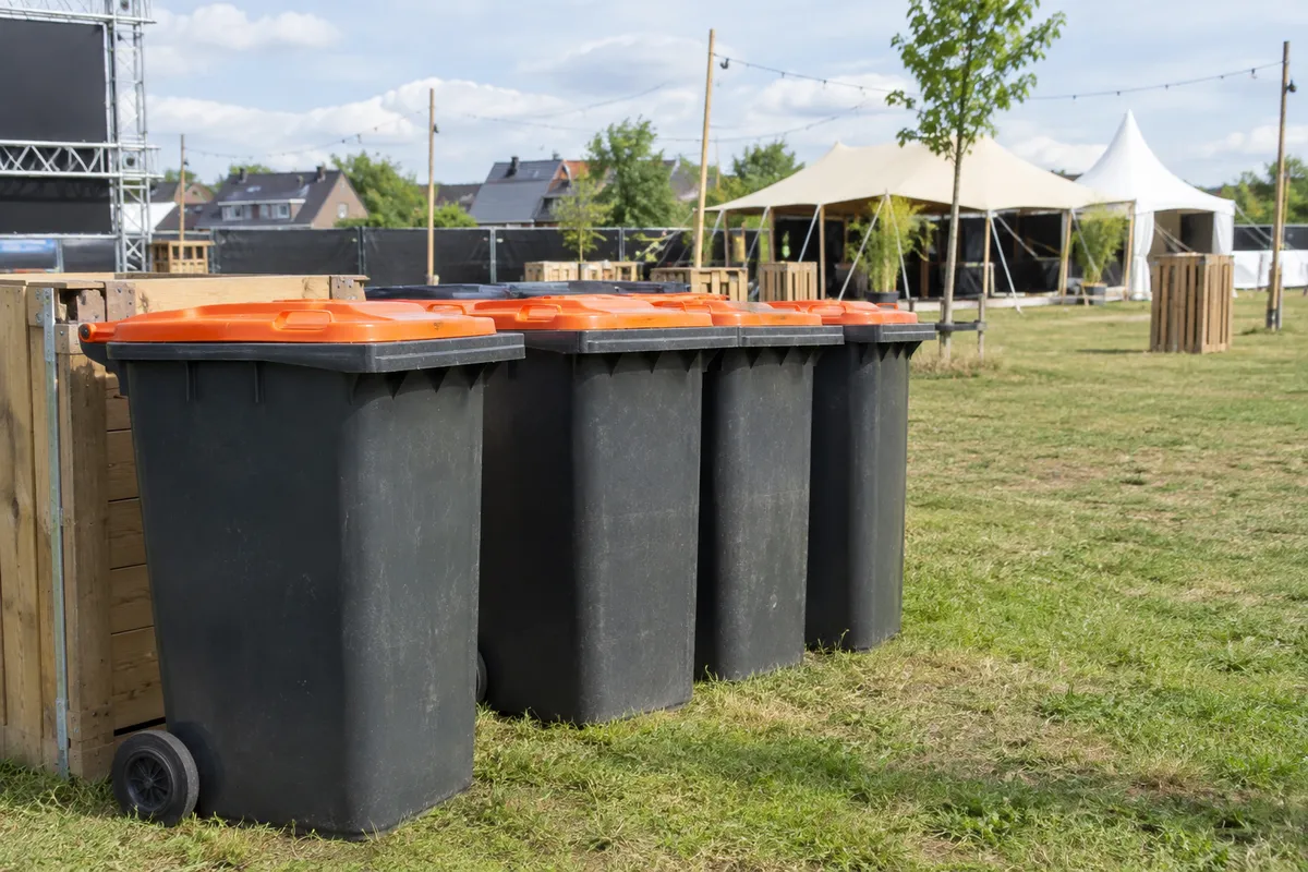 Afvalbakken met oranje deksel op een evenemententerrein
