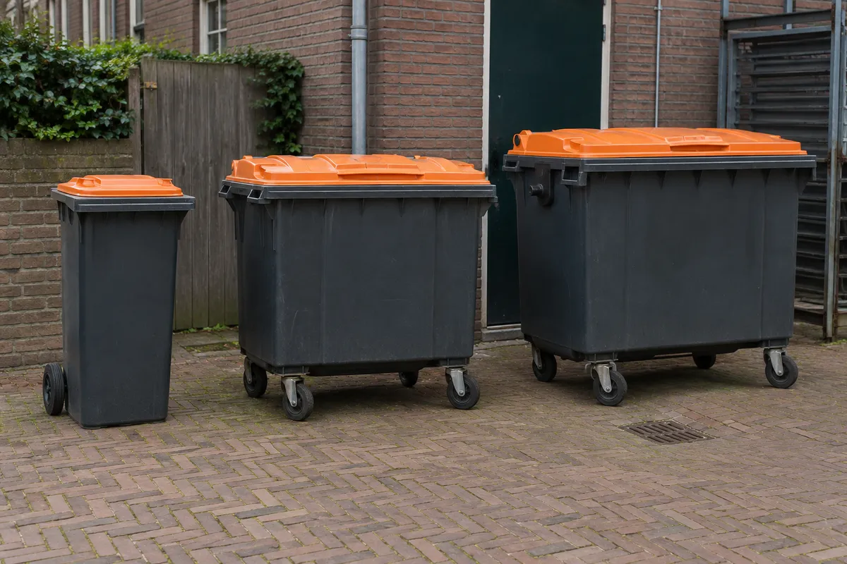 Rolcontainers van 240, 660 en 1100 liter met oranje deksel achter een winkel